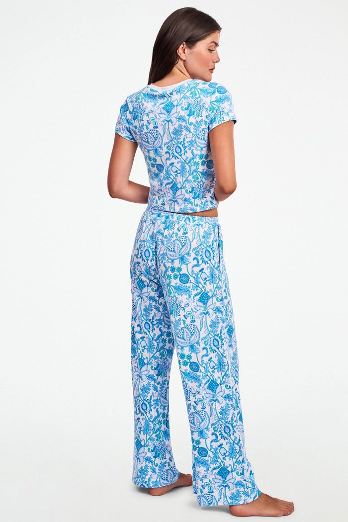 A woman with long brown hair wears the Roller Rabbit Amanda Baby Tee, featuring a blue and turquoise floral and sea-inspired print, standing against a plain white background.