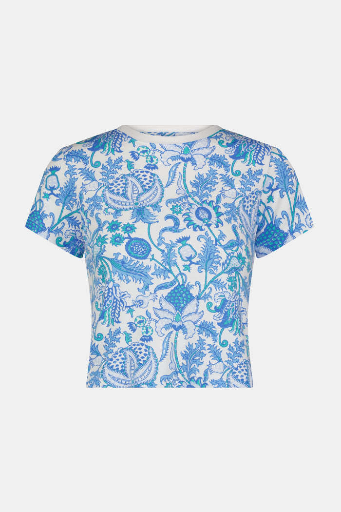 A woman with long brown hair wears the Roller Rabbit Amanda Baby Tee, featuring a blue and turquoise floral and sea-inspired print, standing against a plain white background.