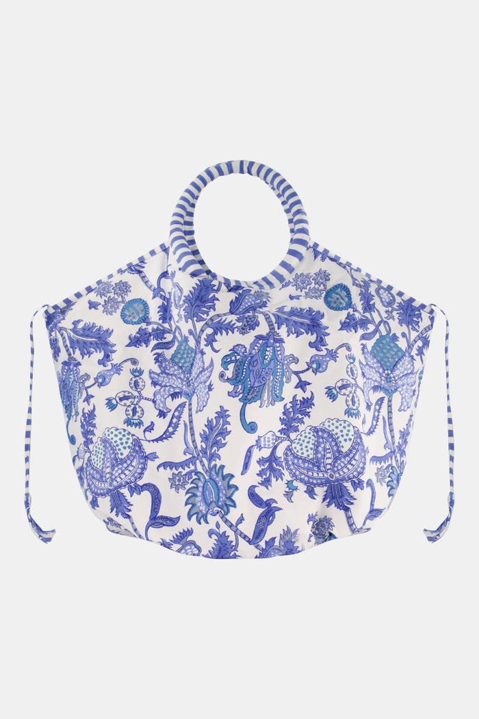 The Amanda Bondi Bag by Roller Rabbit is an oversized canvas tote with circular striped handles, blue floral patterns, side drawstrings, and a wide, rounded shape.