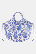 The Amanda Bondi Bag by Roller Rabbit is an oversized canvas tote with circular striped handles, blue floral patterns, side drawstrings, and a wide, rounded shape.