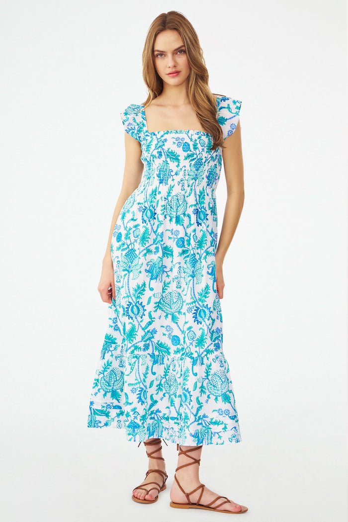 A woman models the Roller Rabbit Amanda Doe Dress—a blue and white cotton voile maxi with flutter sleeves, smocked bodice, and square neckline—paired with brown strappy sandals against a plain white background.