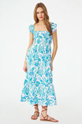 A woman models the Roller Rabbit Amanda Doe Dress—a blue and white cotton voile maxi with flutter sleeves, smocked bodice, and square neckline—paired with brown strappy sandals against a plain white background.