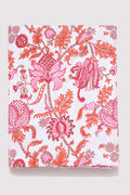 A bed featuring the Roller Rabbit Amanda Duvet Cover, a 300 thread count cotton piece in vibrant pink and orange botanical print, shown with a white carved headboard and white curtains in the background.