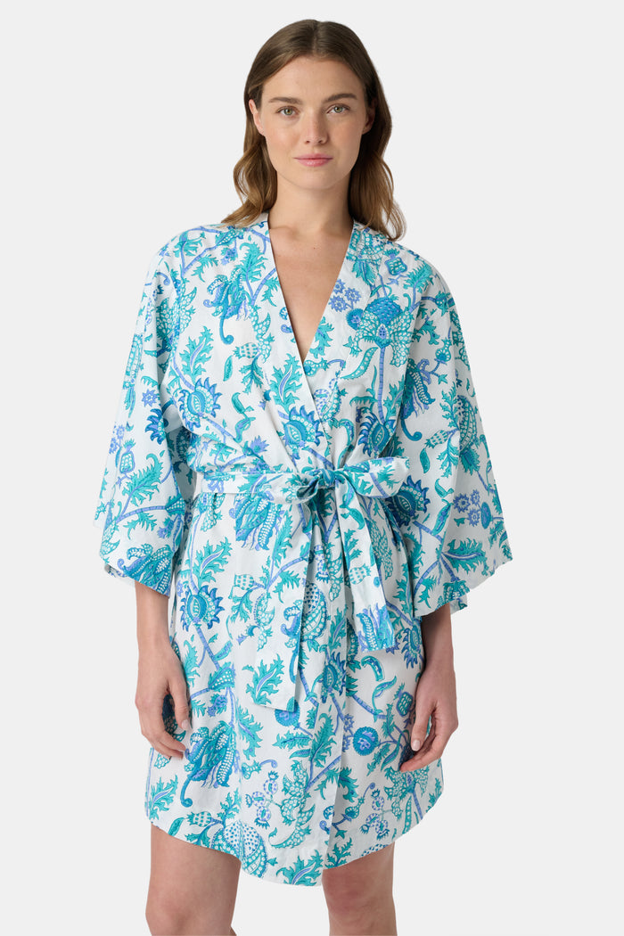 A woman models the Roller Rabbit Amanda Kimono, a knee-length, light blue and white floral cambric cotton robe with wide sleeves and a matching belt, standing against a plain white background.