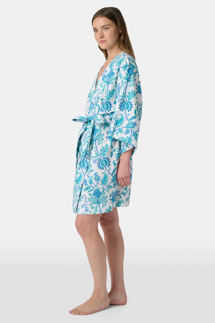 A woman models the Roller Rabbit Amanda Kimono, a knee-length, light blue and white floral cambric cotton robe with wide sleeves and a matching belt, standing against a plain white background.