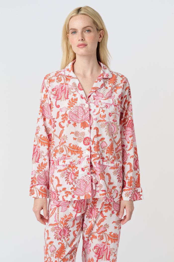 A woman with long blonde hair stands barefoot against a plain background, modeling the Amanda Loungewear by Roller Rabbit—an elegant women's pajama set featuring a white base with red and pink floral prints.