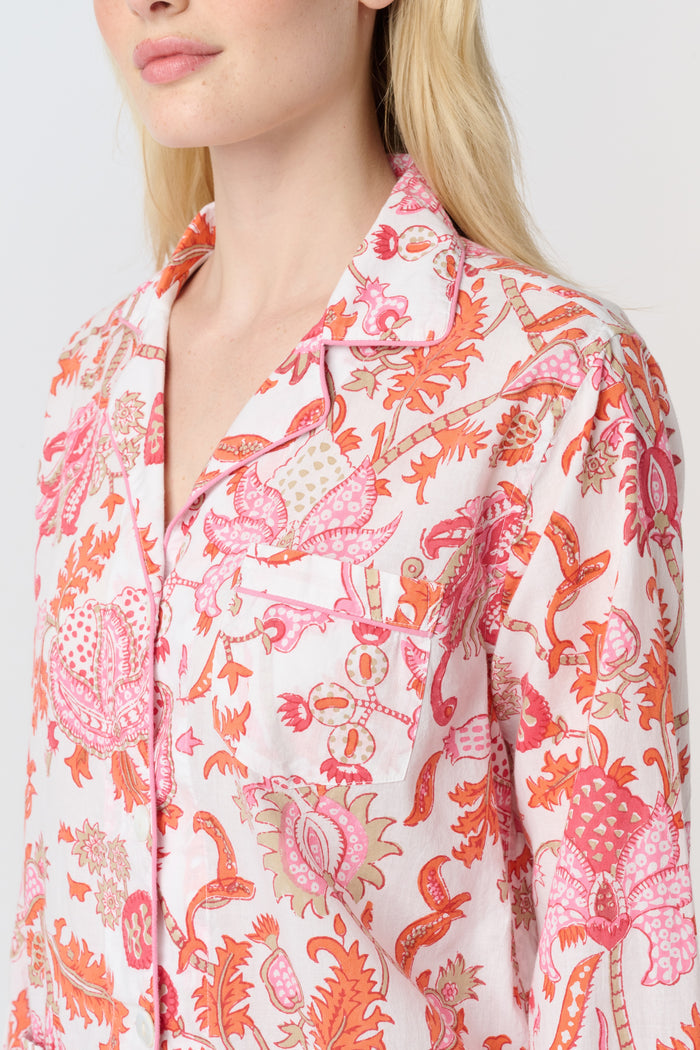 A woman with long blonde hair stands barefoot against a plain background, modeling the Amanda Loungewear by Roller Rabbit—an elegant women's pajama set featuring a white base with red and pink floral prints.