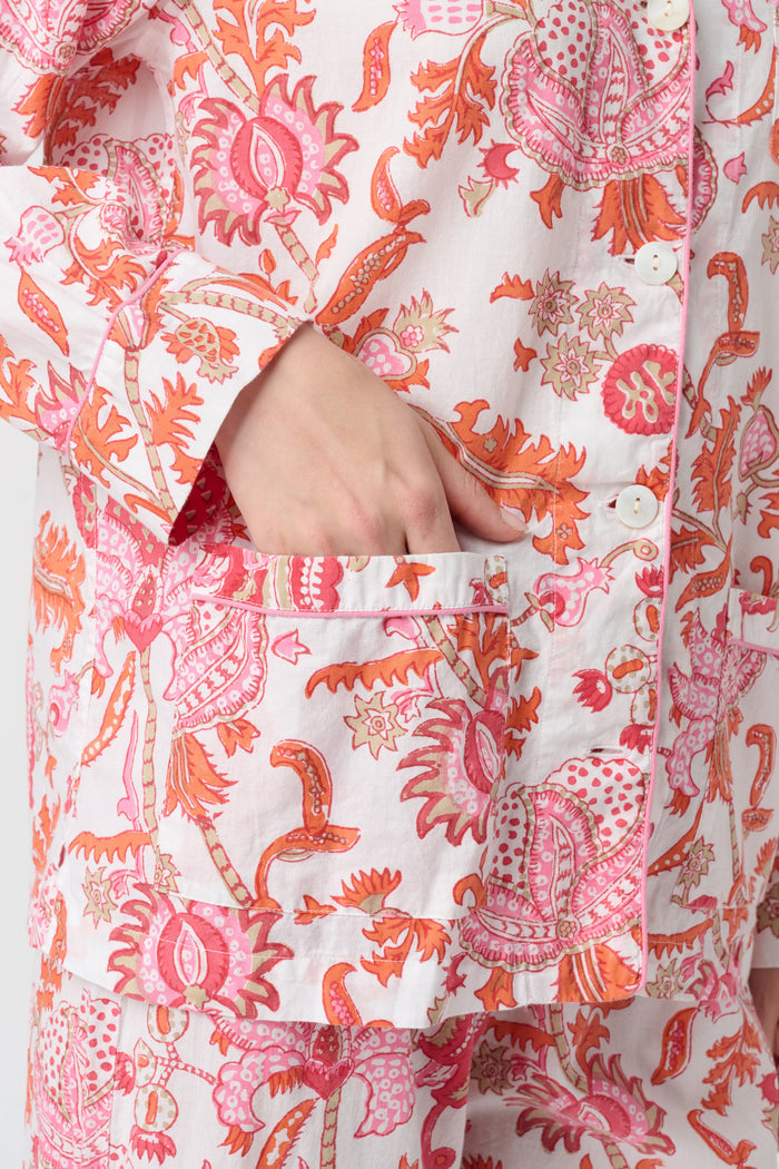 A woman with long blonde hair stands barefoot against a plain background, modeling the Amanda Loungewear by Roller Rabbit—an elegant women's pajama set featuring a white base with red and pink floral prints.