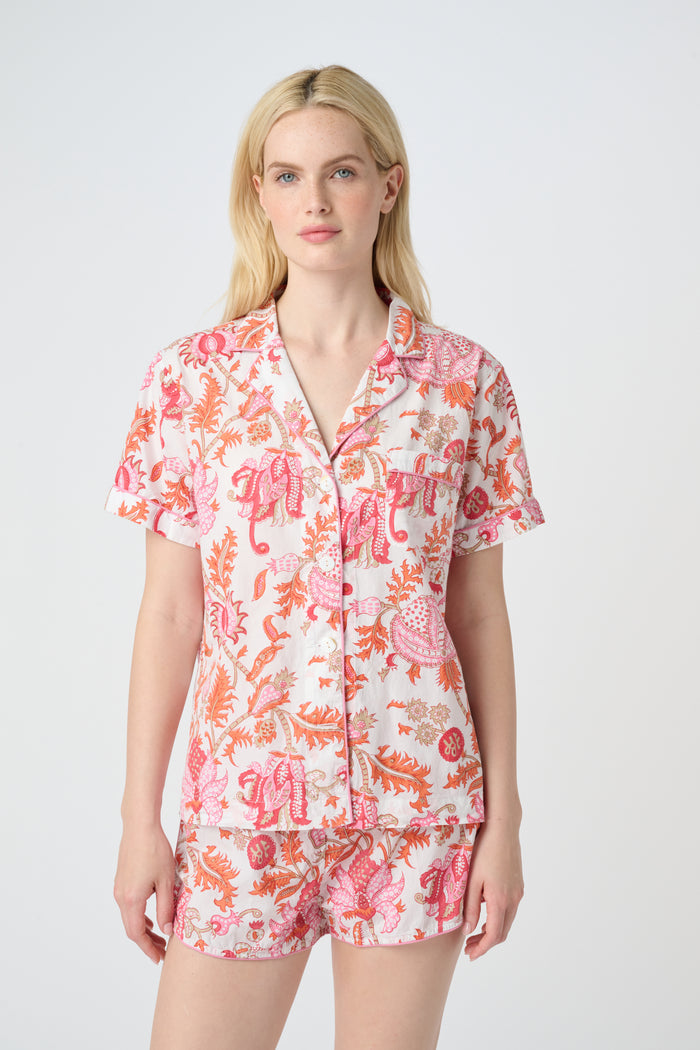 A woman poses against a plain background in the Roller Rabbit Amanda Lulu Set—cotton, short-sleeve, button-up pajamas with matching shorts in a pink and orange floral print.