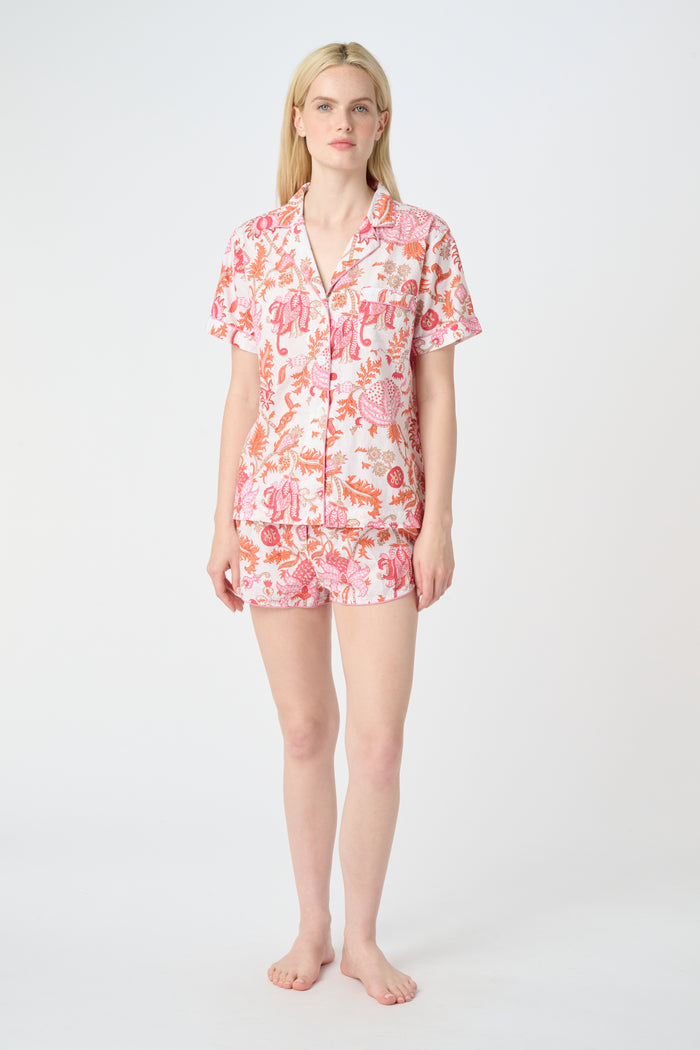 A woman poses against a plain background in the Roller Rabbit Amanda Lulu Set—cotton, short-sleeve, button-up pajamas with matching shorts in a pink and orange floral print.