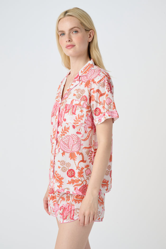 A woman poses against a plain background in the Roller Rabbit Amanda Lulu Set—cotton, short-sleeve, button-up pajamas with matching shorts in a pink and orange floral print.
