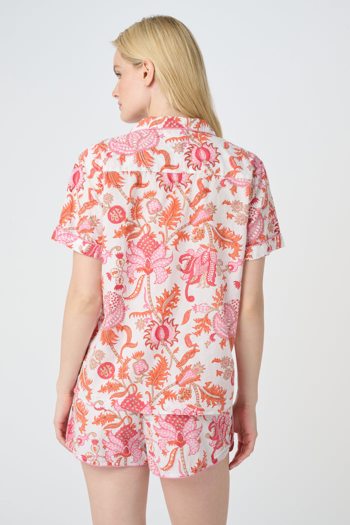 A woman poses against a plain background in the Roller Rabbit Amanda Lulu Set—cotton, short-sleeve, button-up pajamas with matching shorts in a pink and orange floral print.