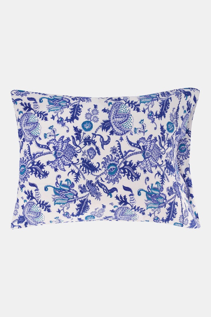 Two pillows on a bed display the Roller Rabbit Amanda Pillowcase Set in blue and white 100 cotton print, matched with sheets. A white, intricately carved headboard serves as the background.