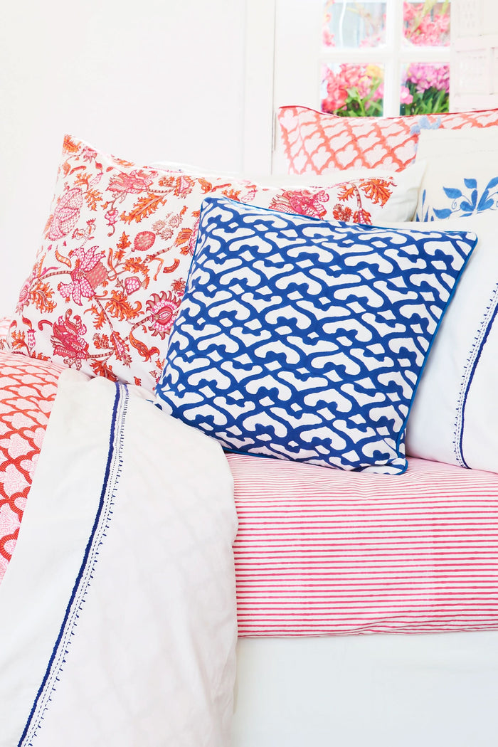Two stacked pillows on a bed showcase the Roller Rabbit Amanda Pillowcase Set, featuring a vibrant red and pink floral and animal print on soft 300 thread count cotton, set against a white decorative headboard.