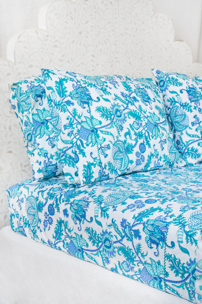 The Amanda Sheet Set by Roller Rabbit features white and blue botanical print bedding and pillowcases, displayed on a white headboard with an intricate leaf design.