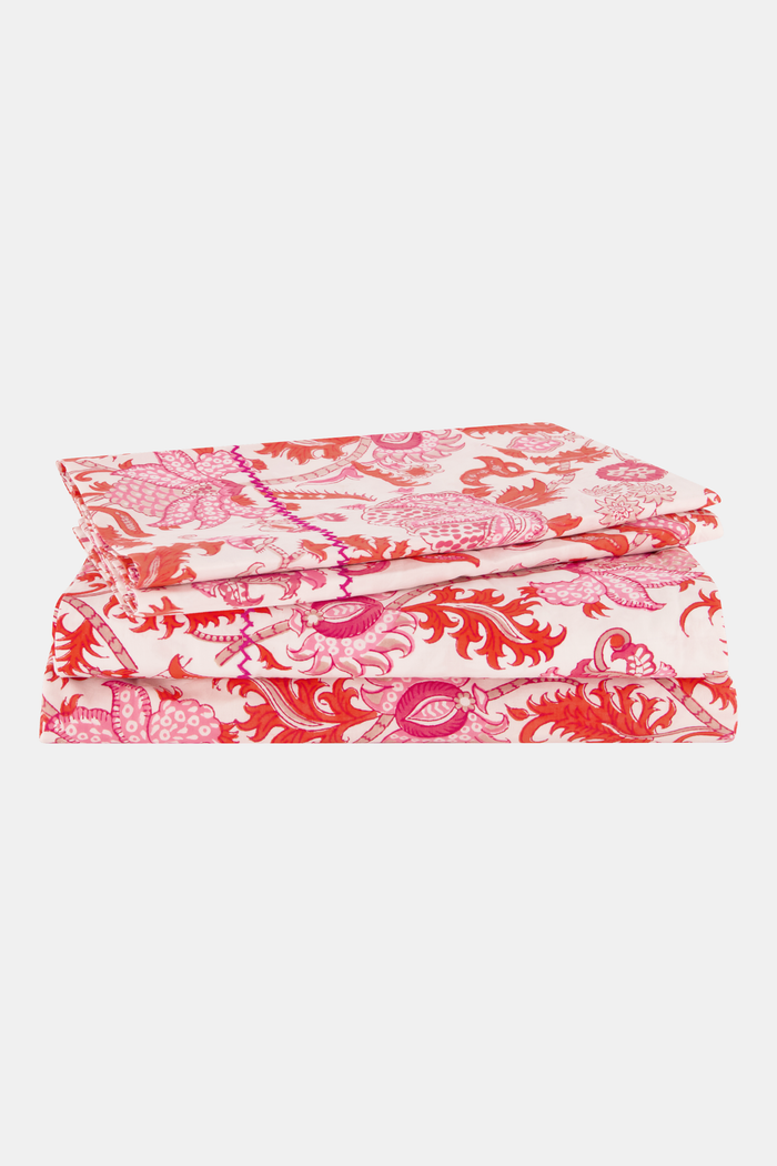 The bed displays the Amanda Sheet Set by Roller Rabbit, featuring white and pink botanical print sheets and pillowcases with intricate red and pink designs. A white headboard with subtle decorative detailing is visible in the background.