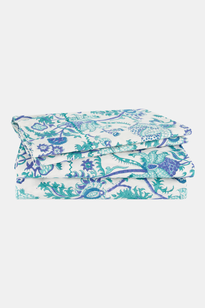 The Amanda Sheet Set by Roller Rabbit features white and blue botanical print bedding and pillowcases, displayed on a white headboard with an intricate leaf design.