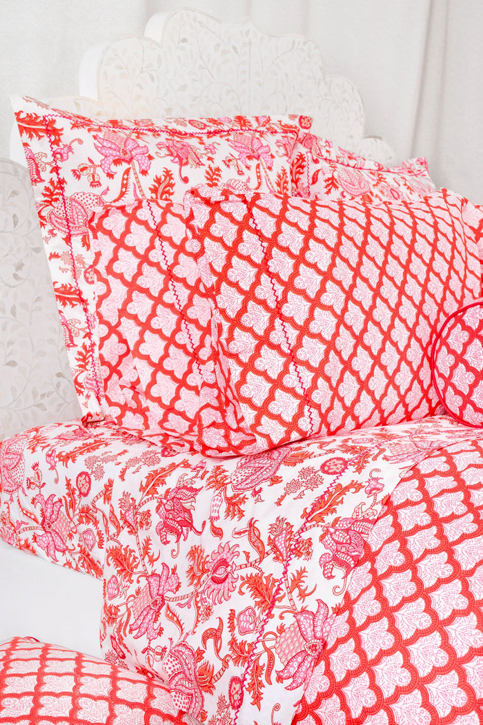 The bed displays the Amanda Sheet Set by Roller Rabbit, featuring white and pink botanical print sheets and pillowcases with intricate red and pink designs. A white headboard with subtle decorative detailing is visible in the background.
