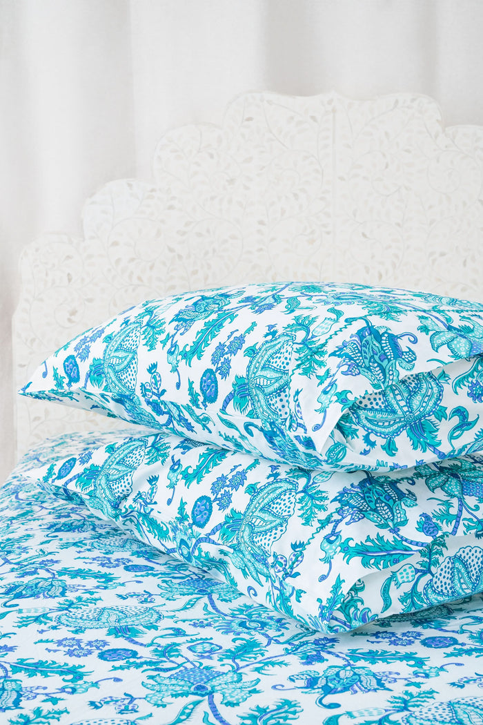 The Amanda Sheet Set by Roller Rabbit features white and blue botanical print bedding and pillowcases, displayed on a white headboard with an intricate leaf design.