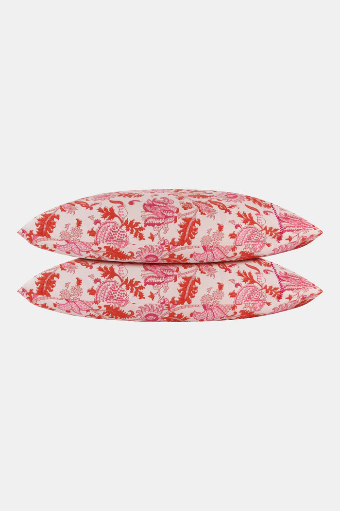 The bed displays the Amanda Sheet Set by Roller Rabbit, featuring white and pink botanical print sheets and pillowcases with intricate red and pink designs. A white headboard with subtle decorative detailing is visible in the background.