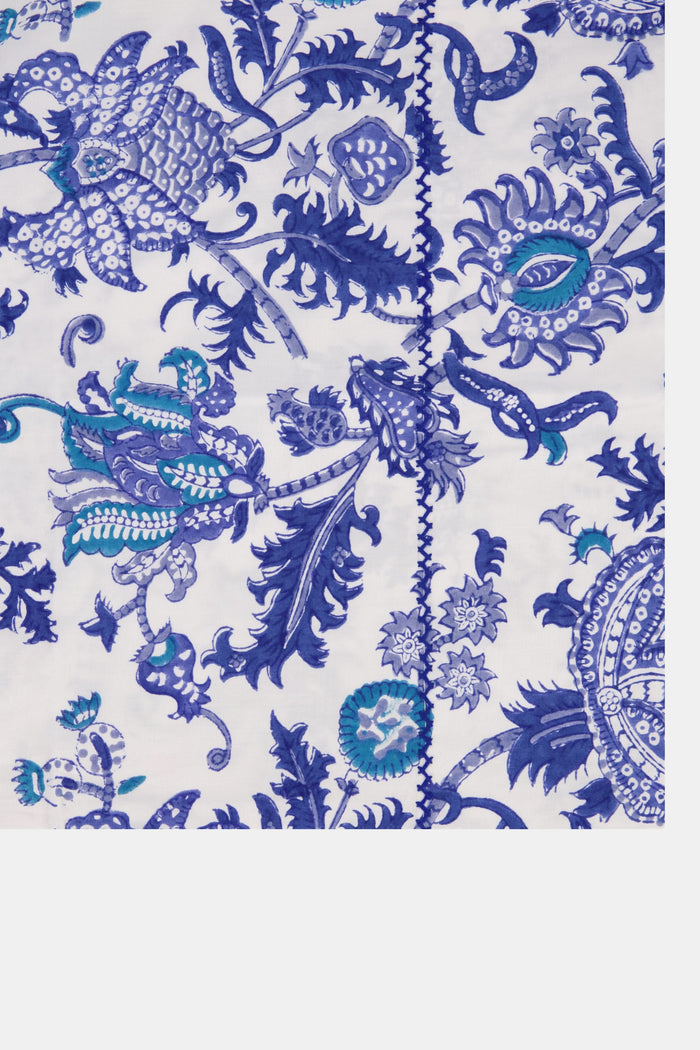 A bed dressed in the Amanda Sheet Set by Roller Rabbit, featuring white and blue botanical prints with intricate designs, is set against a white ornate headboard with a scalloped edge.