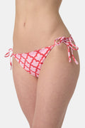 A person wears the Roller Rabbit Amanda/Jemina Serena Bikini Bottom, featuring UPF 50+ protection, white heart-shaped patterns, and side tie strings, shown from waist to mid-thigh against a plain background.
