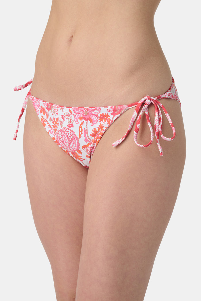 A person wears the Roller Rabbit Amanda/Jemina Serena Bikini Bottom, featuring UPF 50+ protection, white heart-shaped patterns, and side tie strings, shown from waist to mid-thigh against a plain background.