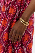 A close-up of a person’s hand wearing the Roller Rabbit Bamboo Bangle Set, resting against a dress with a bold geometric red, orange, and white pattern.
