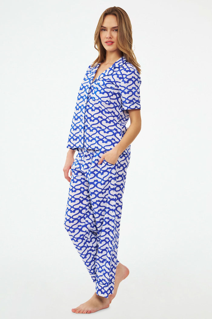 A woman stands barefoot in the Roller Rabbit Big Cata Liza Set, a matching short-sleeve pajama set made from cambric cotton with a blue and white Big Cata print, posing against a plain white background.