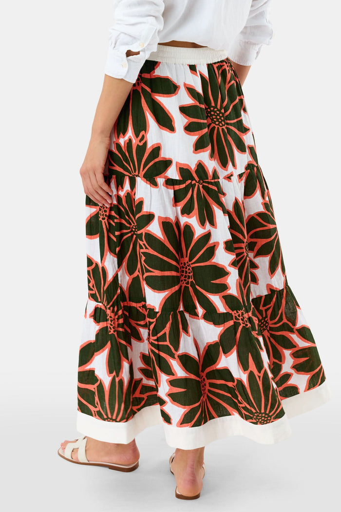 A person wears a white Roller Rabbit Blooming Daisies Carlisa Skirt with bold black and orange floral prints, paired with a white top and white sandals.