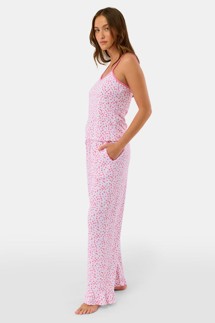 A woman faces forward, barefoot against a plain white background, wearing the Roller Rabbit Bouquet Lily Set—a pink and white polka dot pajama with a sleeveless top and long pants made from soft Pima Soft fabric.