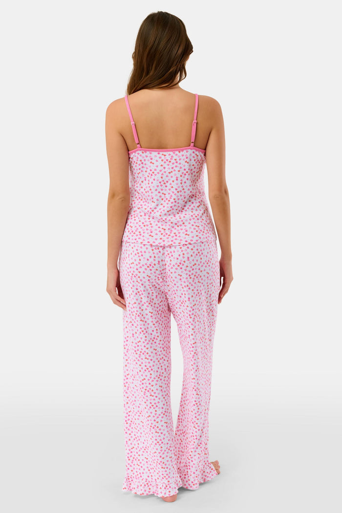 A woman faces forward, barefoot against a plain white background, wearing the Roller Rabbit Bouquet Lily Set—a pink and white polka dot pajama with a sleeveless top and long pants made from soft Pima Soft fabric.