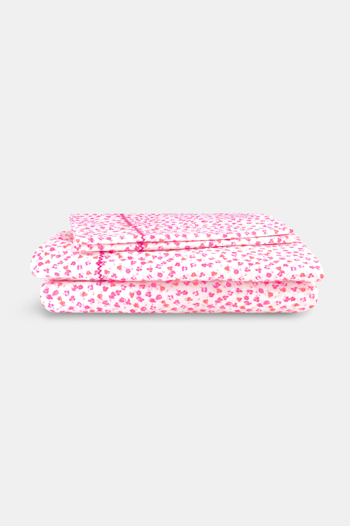 The bed features Roller Rabbit’s Bouquet Sheet Set, with a white ornate headboard and light pink 300 thread count cotton sheets and pillowcases adorned with small hearts and decorative pink stitching for a soft, cozy look.