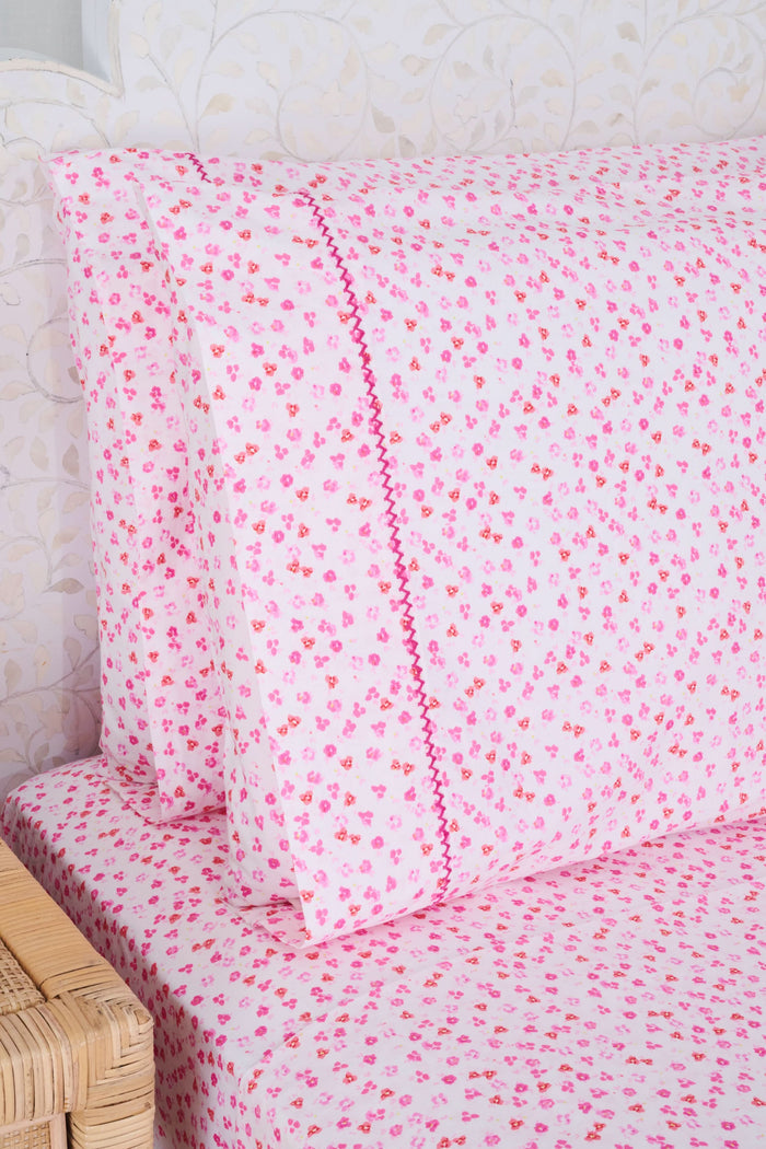 The bed features Roller Rabbit’s Bouquet Sheet Set, with a white ornate headboard and light pink 300 thread count cotton sheets and pillowcases adorned with small hearts and decorative pink stitching for a soft, cozy look.