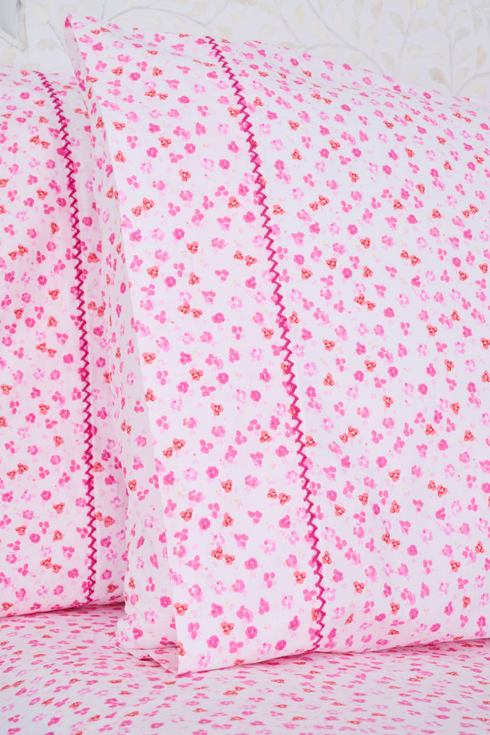 The bed features Roller Rabbit’s Bouquet Sheet Set, with a white ornate headboard and light pink 300 thread count cotton sheets and pillowcases adorned with small hearts and decorative pink stitching for a soft, cozy look.