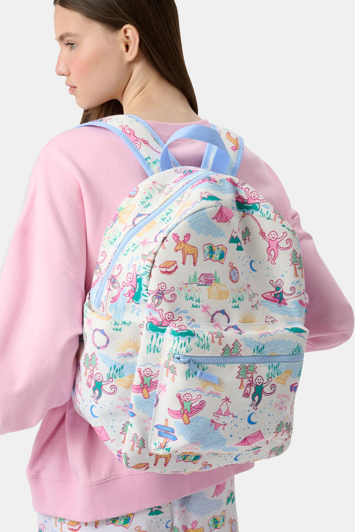 The Camp RR Backpack by Roller Rabbit features colorful cartoon camping scenes—mountains, animals, tents, trees, and rivers—plus playful characters in pink, blue, yellow, and green.