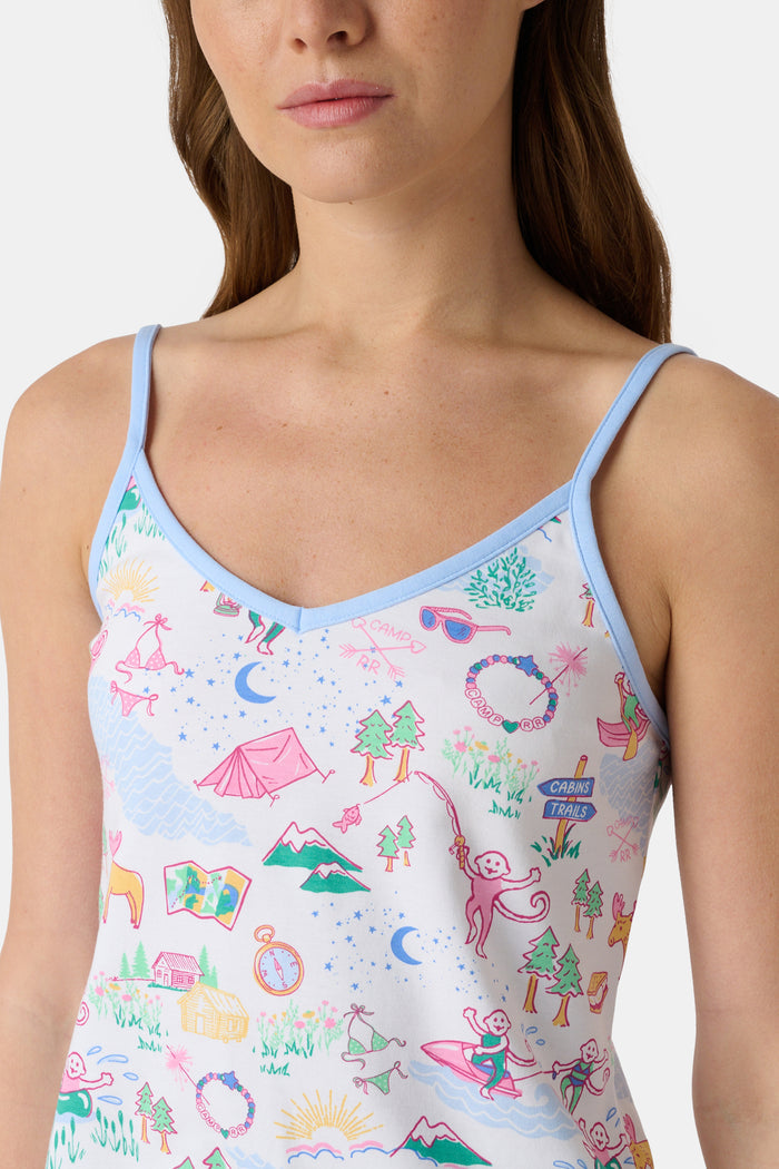 A woman with long brown hair wears the Roller Rabbit Camp RR Mischa Set, a light-hued Pima cotton pajama set with playful prints. The adjustable strap tank and shorts provide comfort as she stands turned slightly to the side, gazing off-camera.