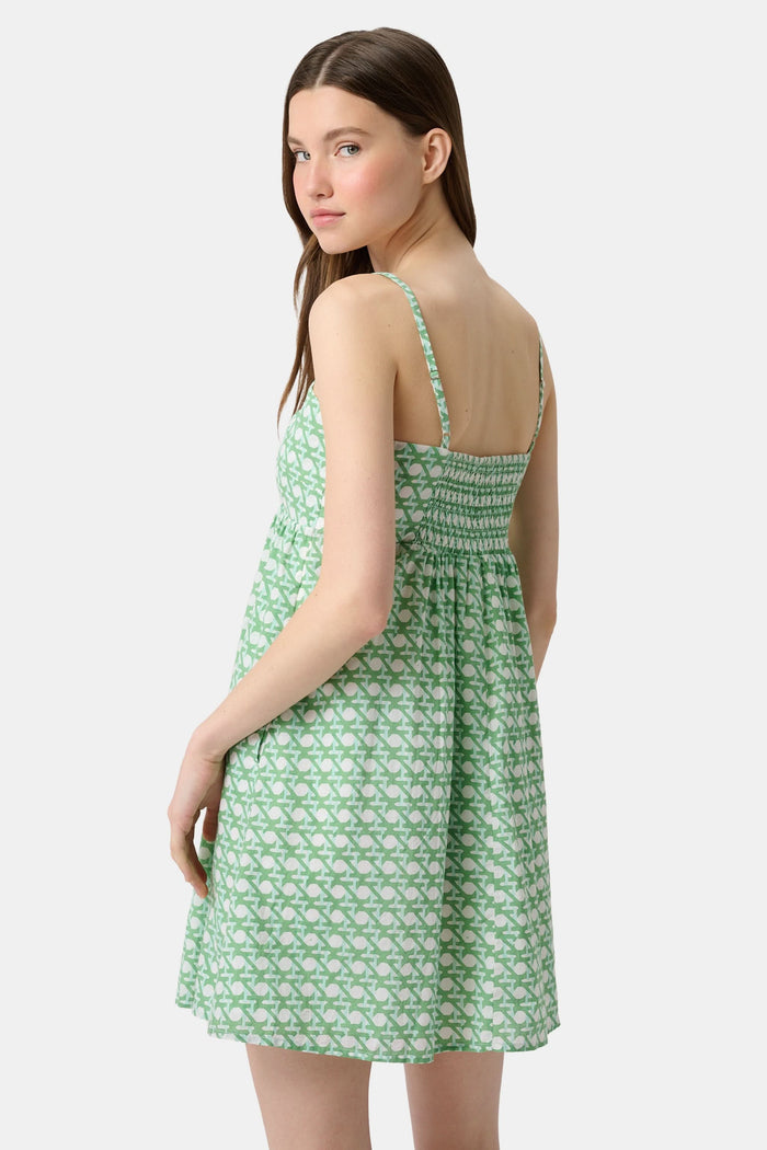 A woman with long curly hair wears the Roller Rabbit Cane Sofie Dress in kelly green, standing outdoors on grass by a hedge, with boats and water in the background.