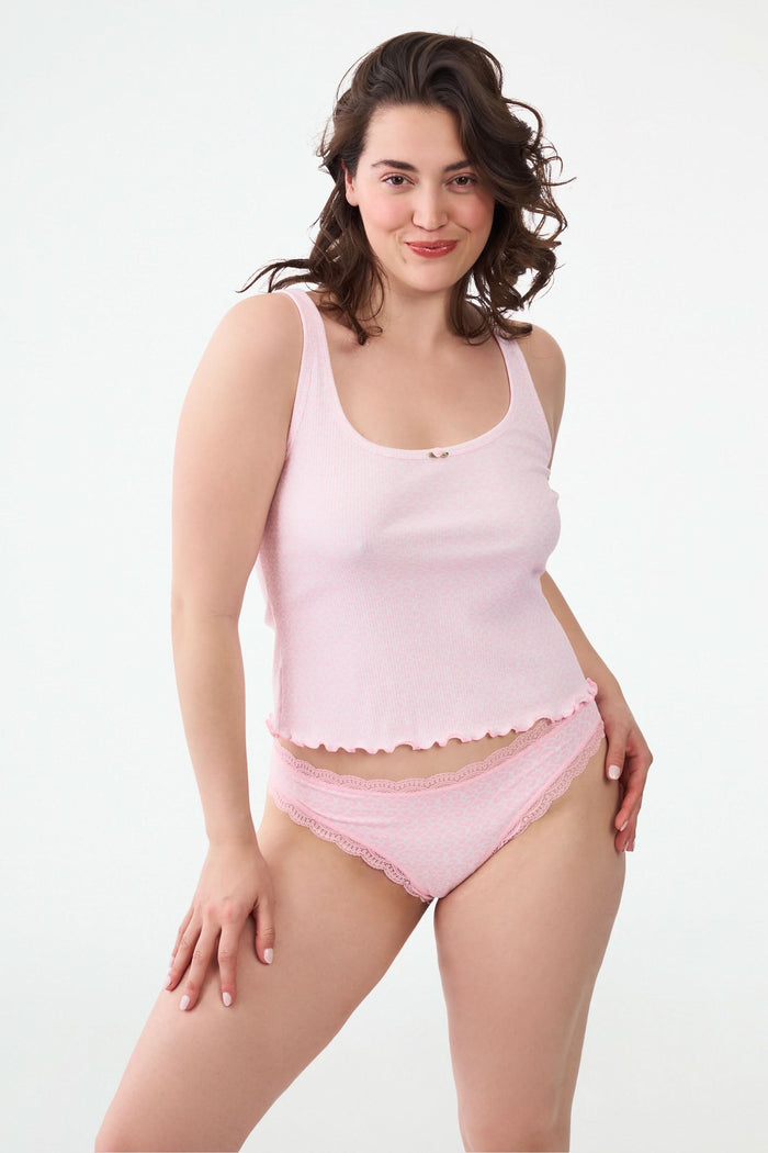 A woman wears the Roller Rabbit Catalina Rib Astor Tank in light pink with a small neckline bow and matching high-waisted button shorts. Against a plain background, her curly hair frames her face as she models these chic party PJs.