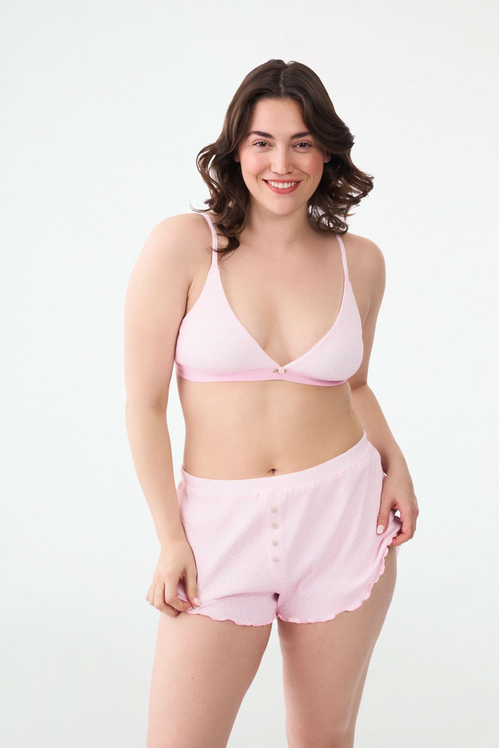 A person wears the Roller Rabbit Catalina Rib Sullivan Shortie set—light pink ribbed tank top and matching boxer-inspired shorts with ruffled hems and decorative buttons—against a plain white background.