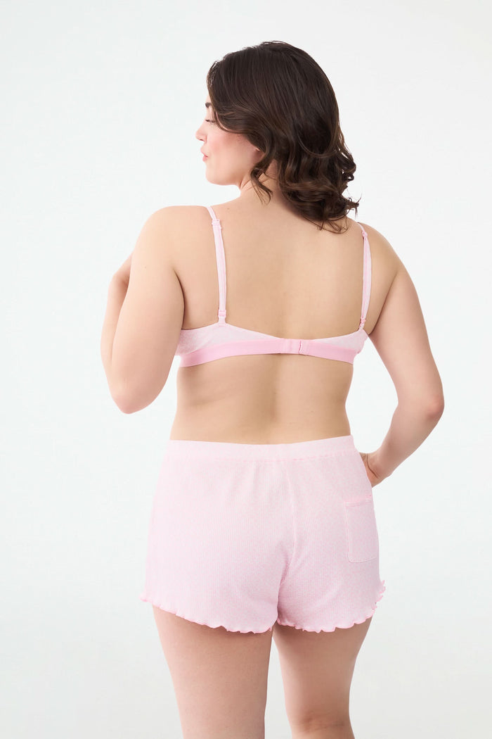 A person wears the Roller Rabbit Catalina Rib Sullivan Shortie set—light pink ribbed tank top and matching boxer-inspired shorts with ruffled hems and decorative buttons—against a plain white background.