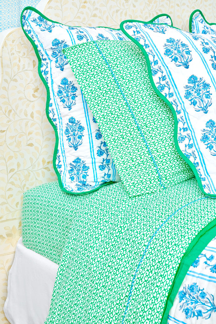 A close-up of a bed with green and white patterned Catalina Sheet Set from Roller Rabbit and a matching pillow with blue floral trim. The pale beige headboard features a floral pattern, adding style to this cozy 300-thread-count cotton bedding.