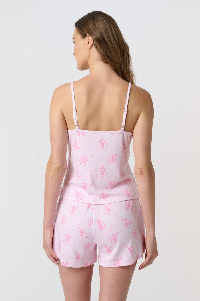 A woman models the Roller Rabbit Cupid's Kiss Cami Boxer Set—a soft Pima cotton pajama set in light pink with a floral pattern, featuring spaghetti straps and matching shorts—standing against a plain white background and smiling gently at the camera.