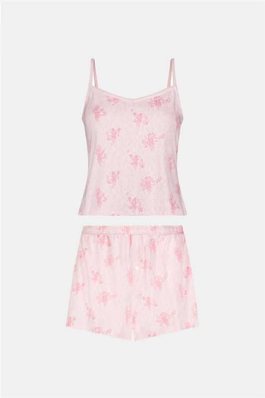 A woman models the Roller Rabbit Cupid's Kiss Cami Boxer Set—a soft Pima cotton pajama set in light pink with a floral pattern, featuring spaghetti straps and matching shorts—standing against a plain white background and smiling gently at the camera.