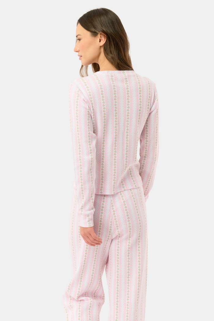 A woman wears the Roller Rabbit Daisy Heart Stripe Rosemary Top with pink, green, and white stripes, featuring a long-sleeved henley design, against a plain light background.