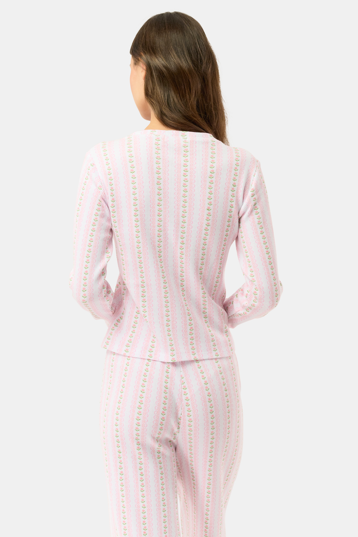 A woman wears the Roller Rabbit Daisy Heart Stripe Rosemary Top with pink, green, and white stripes, featuring a long-sleeved henley design, against a plain light background.