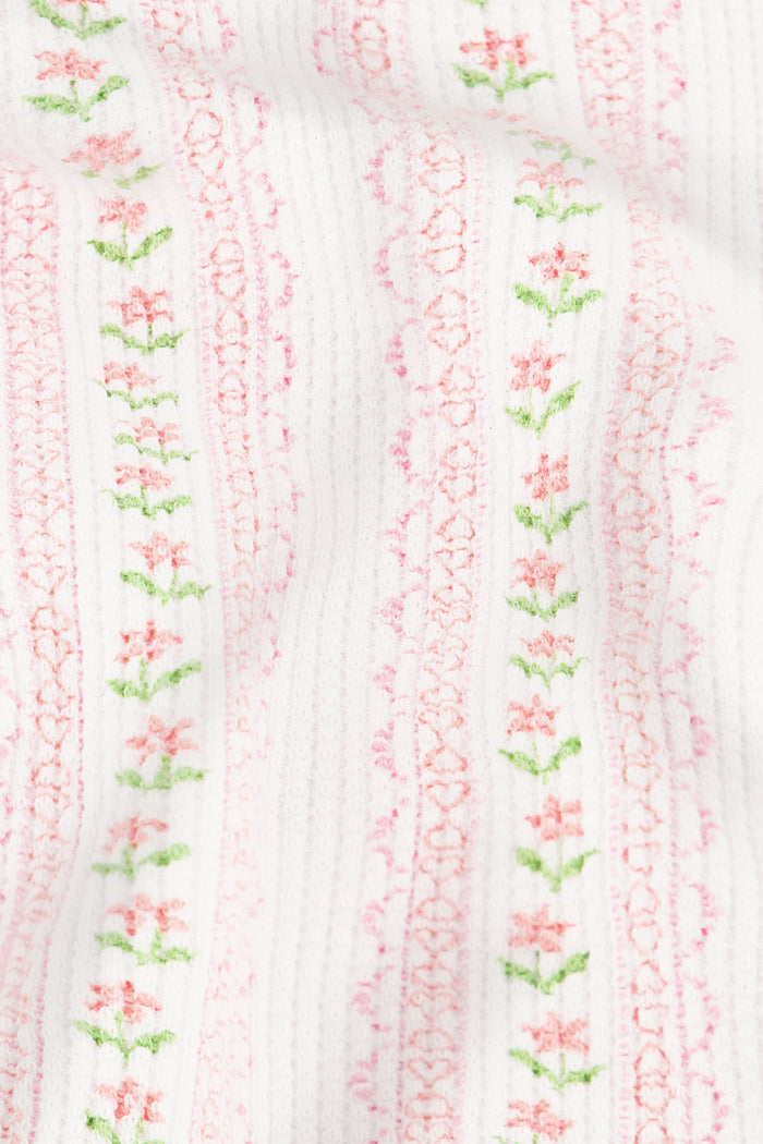 A woman with long, wavy brown hair stands barefoot in a relaxed pose wearing Roller Rabbit’s Daisy Heart Stripe Julienne Pant set—long-sleeve top and loose pants with vertical pastel stripes—against a plain white background.