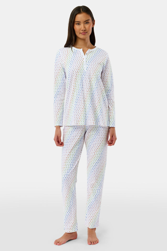 A woman stands barefoot in Roller Rabbit’s Disco Hearts Pajamas, featuring a long-sleeved, buttoned top and straight-leg pants with colorful polka dots on white for comfort and style.