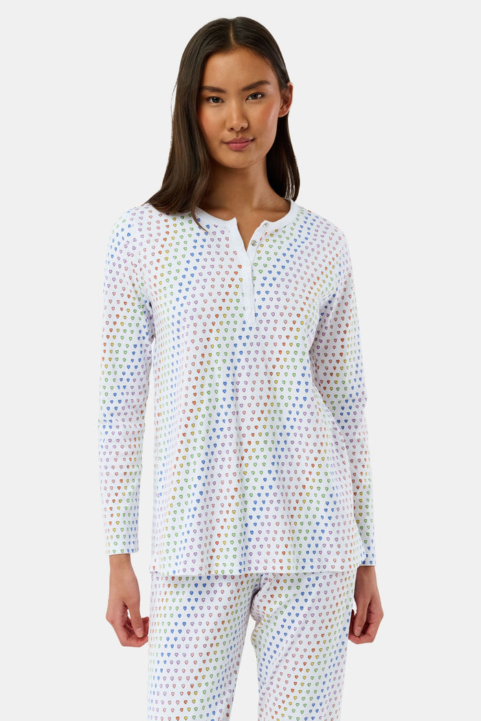 A woman stands barefoot in Roller Rabbit’s Disco Hearts Pajamas, featuring a long-sleeved, buttoned top and straight-leg pants with colorful polka dots on white for comfort and style.