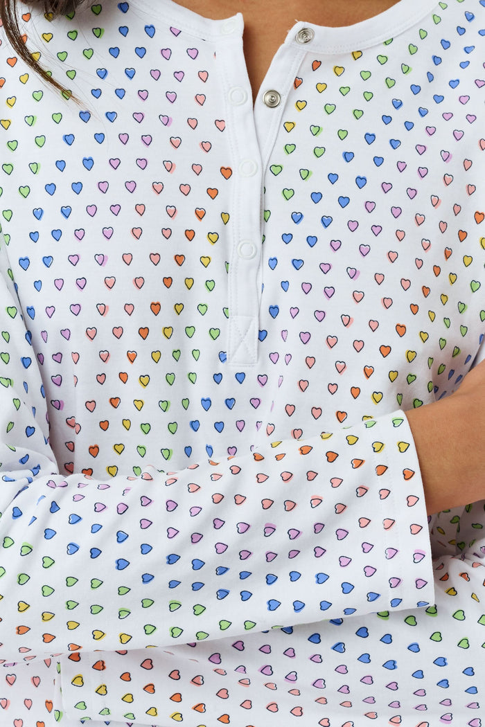 A woman stands barefoot in Roller Rabbit’s Disco Hearts Pajamas, featuring a long-sleeved, buttoned top and straight-leg pants with colorful polka dots on white for comfort and style.